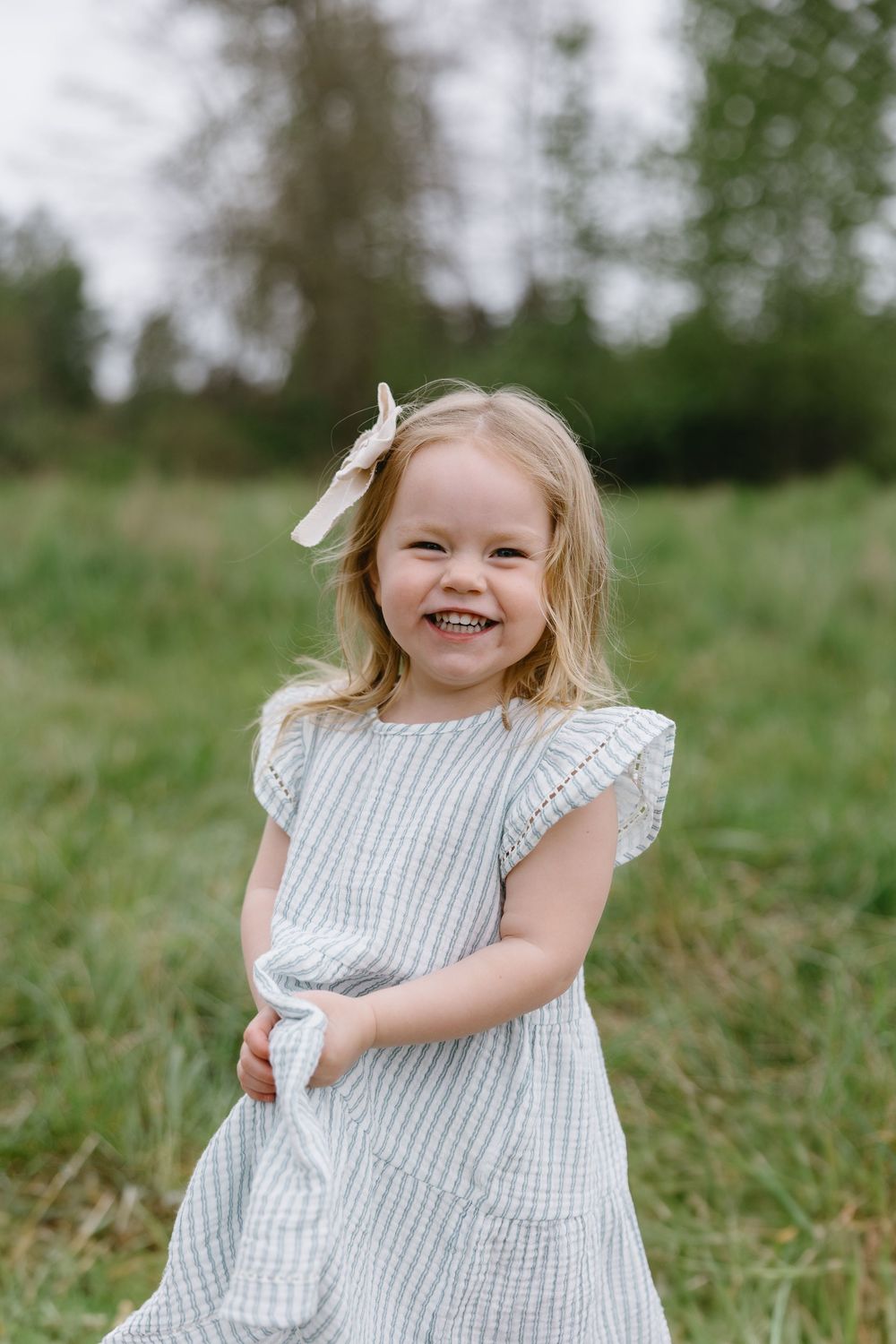 A joyful child in a white sleeveless dress sits in a green grassy field during summer.