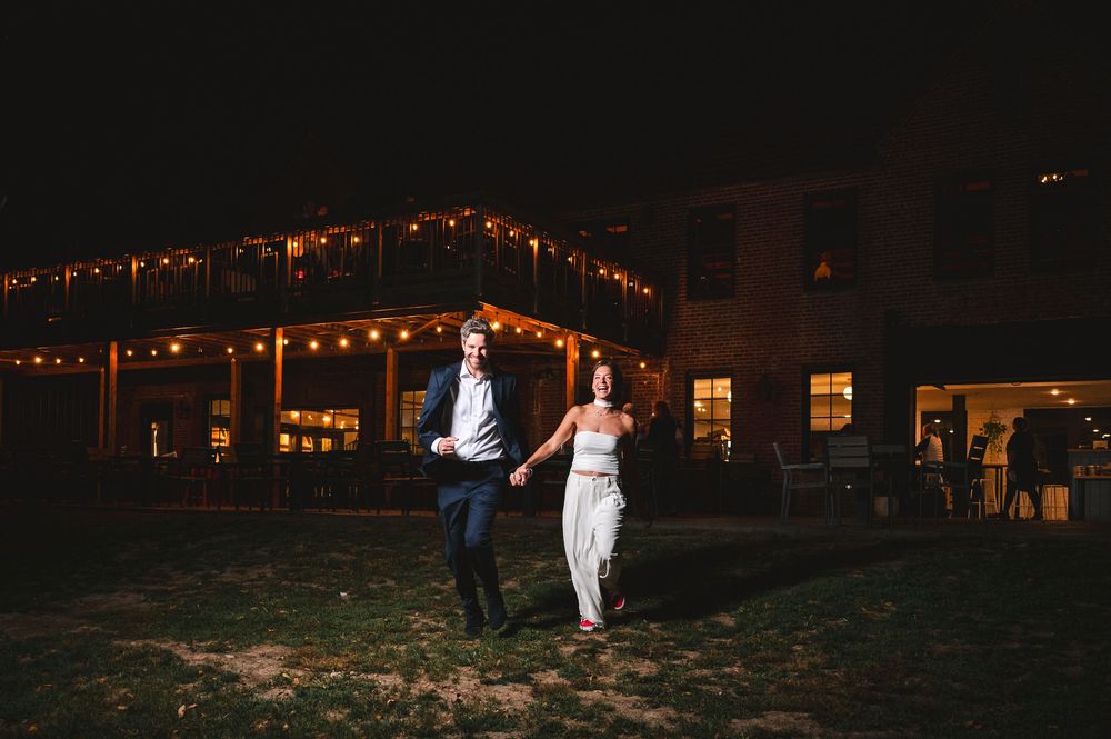 Bride and groom running together against a dark exterior of a brick building at night at Drowned Lands Brewery in Warwick, NY.