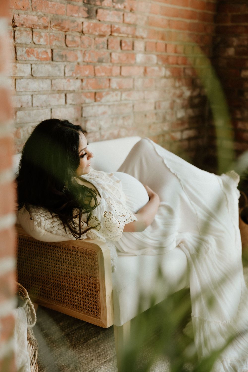 A dreamy bridal portrait with lace dress against rustic brick wall, with soft lighting filtering through greenery.