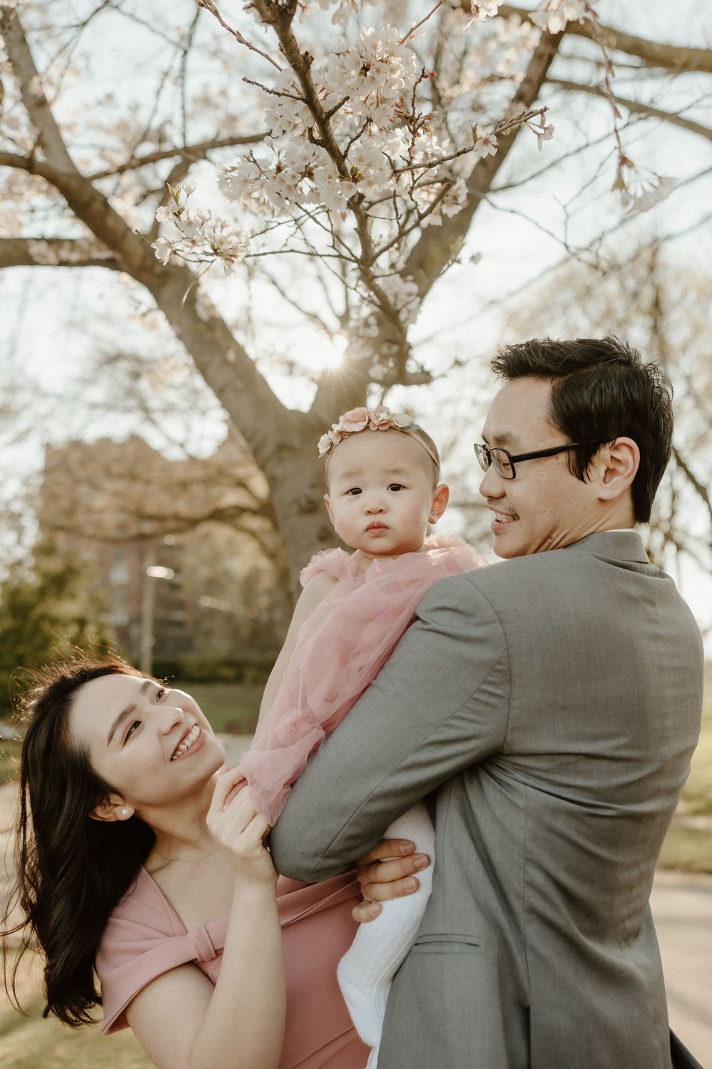 A family enjoys a tender moment together under blooming cherry blossoms on a bright spring day.