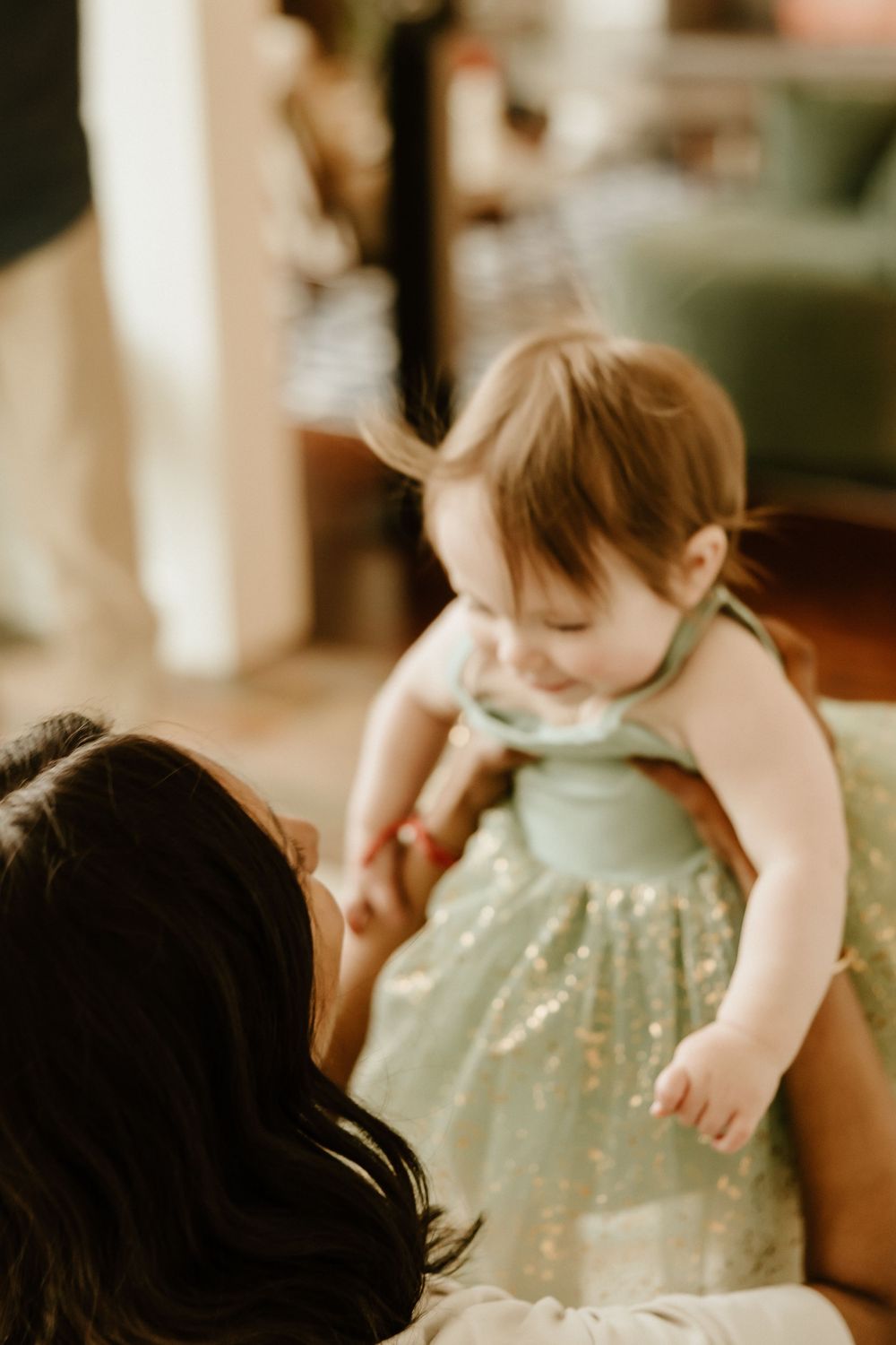 A small child in a sparkly mint green dress being lifted up while smiling joyfully.