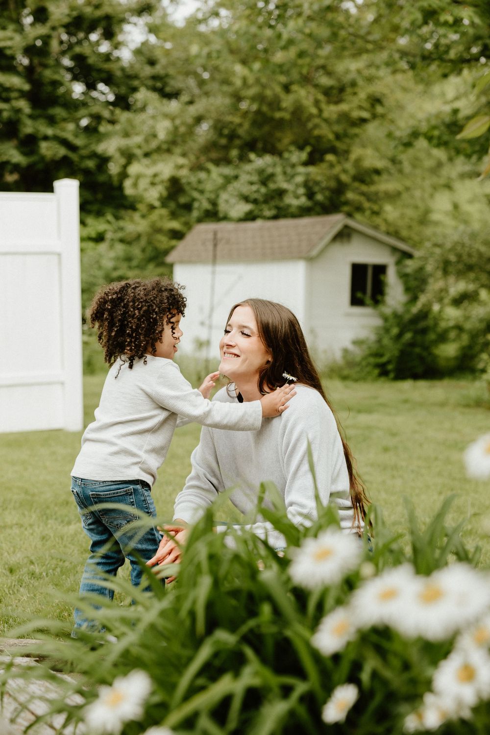 Two people share a joyful moment in a sunny backyard garden with white daisies in the foreground.