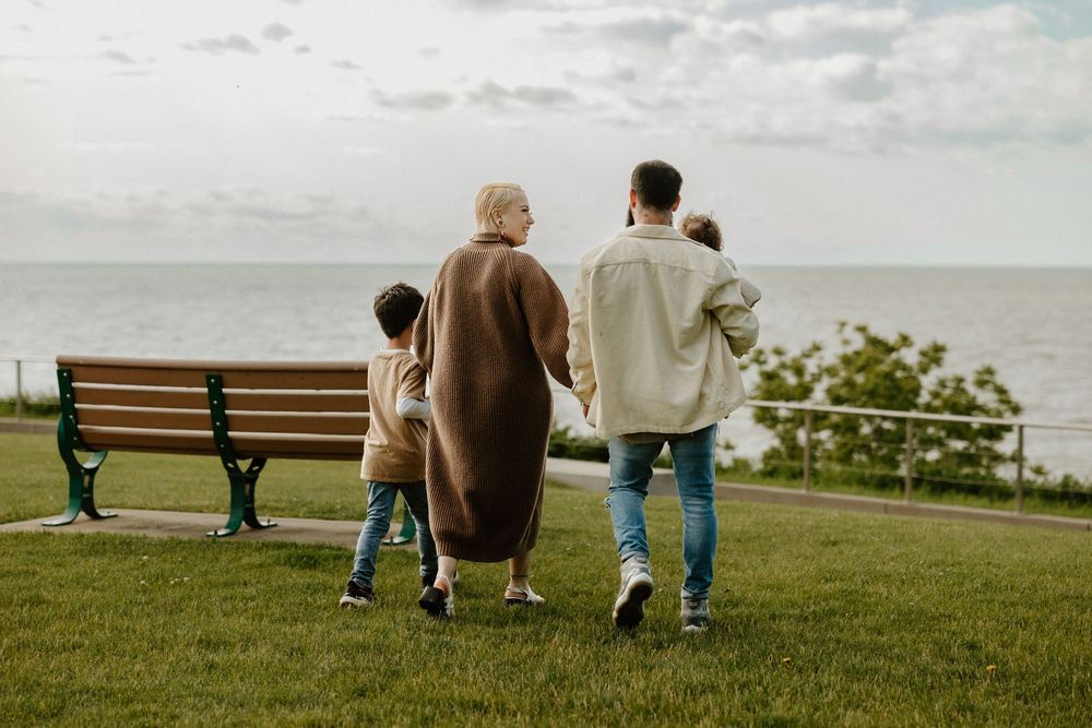 People sit on benches at a scenic overlook along the coastline with a cloudy sky in view.