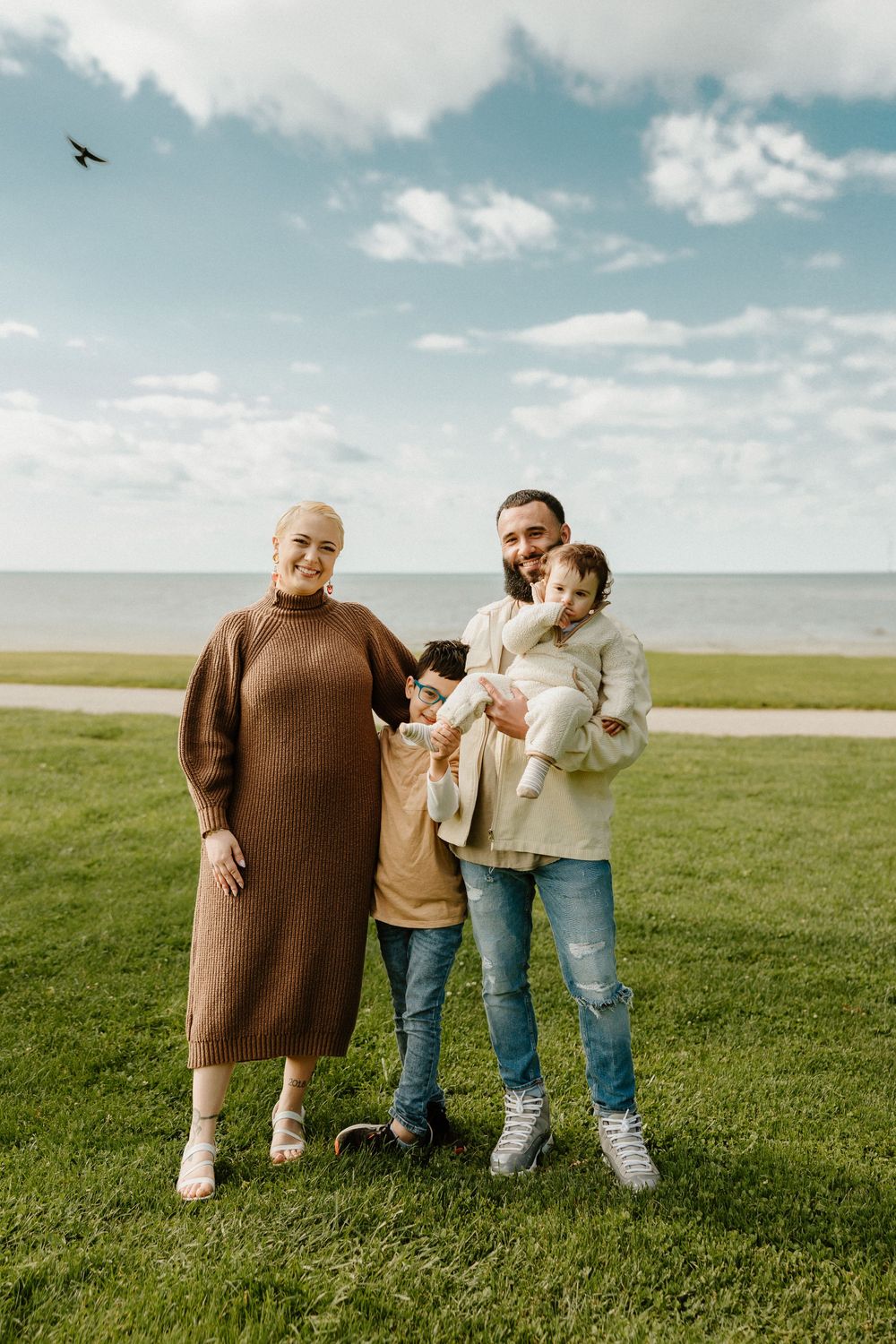A multi-generational group stands together on green grass overlooking the ocean on a cloudy day.