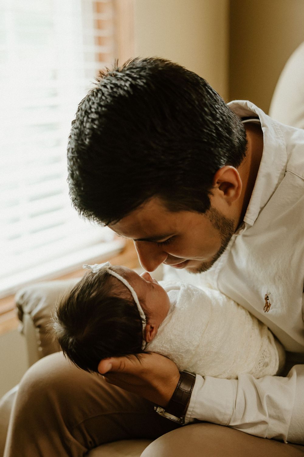 A tender parenting moment shows a gentle forehead kiss while wearing a white button-down shirt in warm natural lighting.