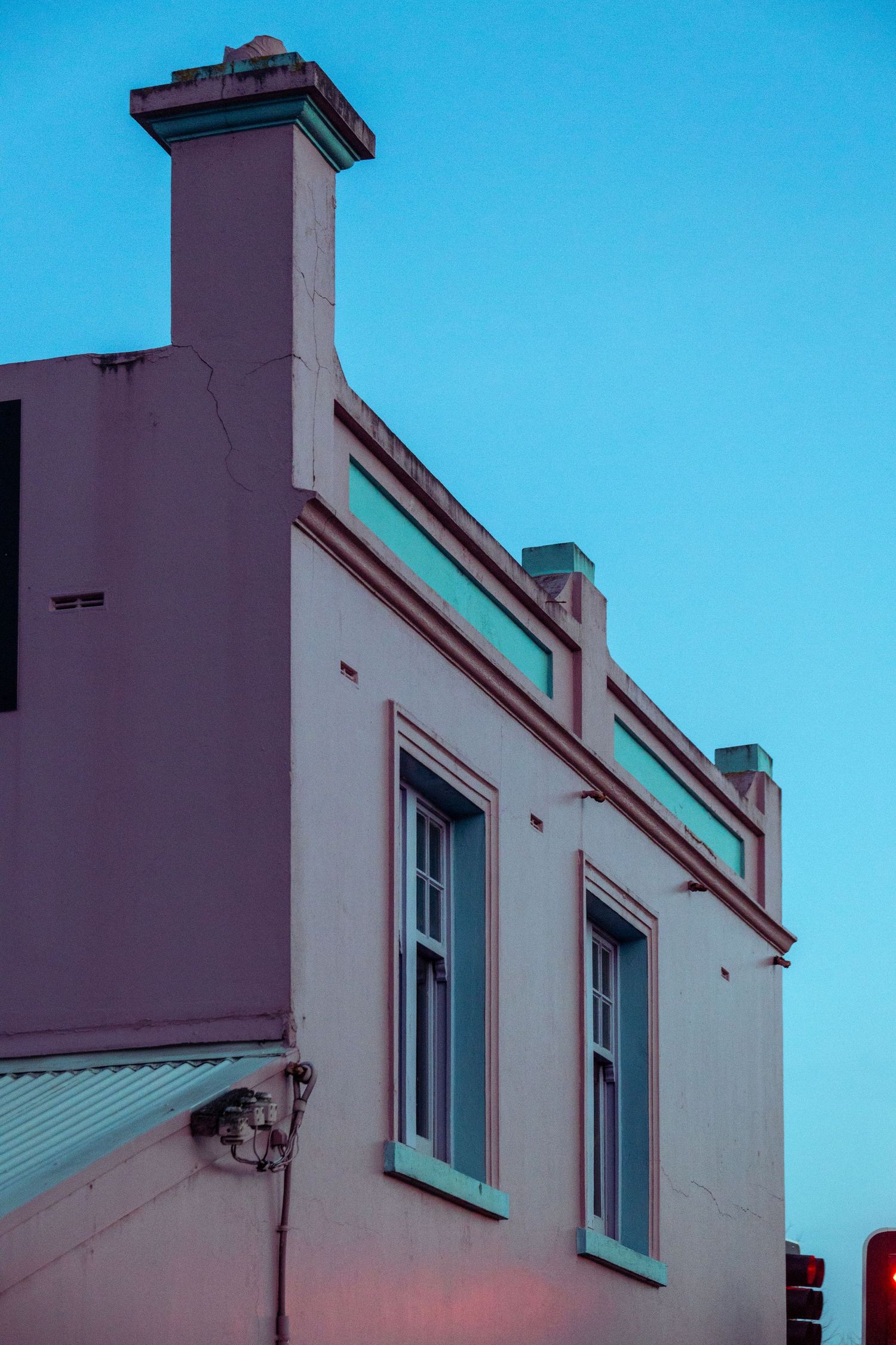 Pink and aqua-painted corner building lit with soft afternoon glow under a deepening teal sky.