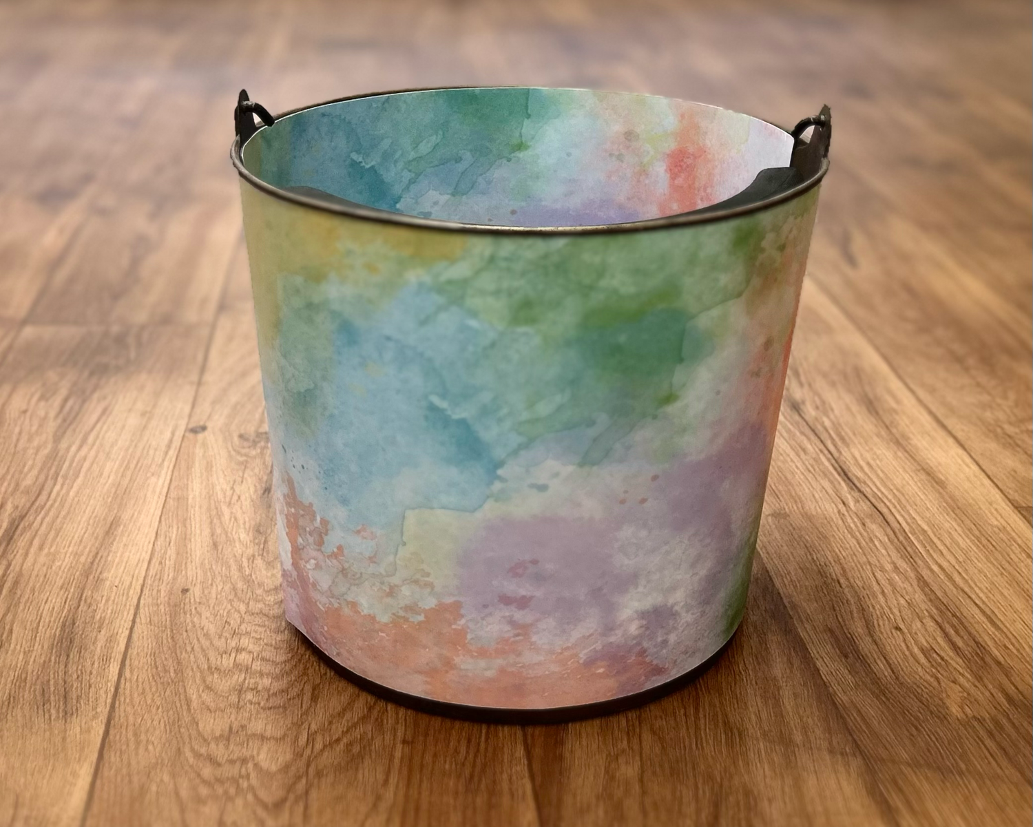 Sleeping newborn rests on colorful tie-dye bucket wearing rainbow flower headband and wrapped in knit rainbow blanket.