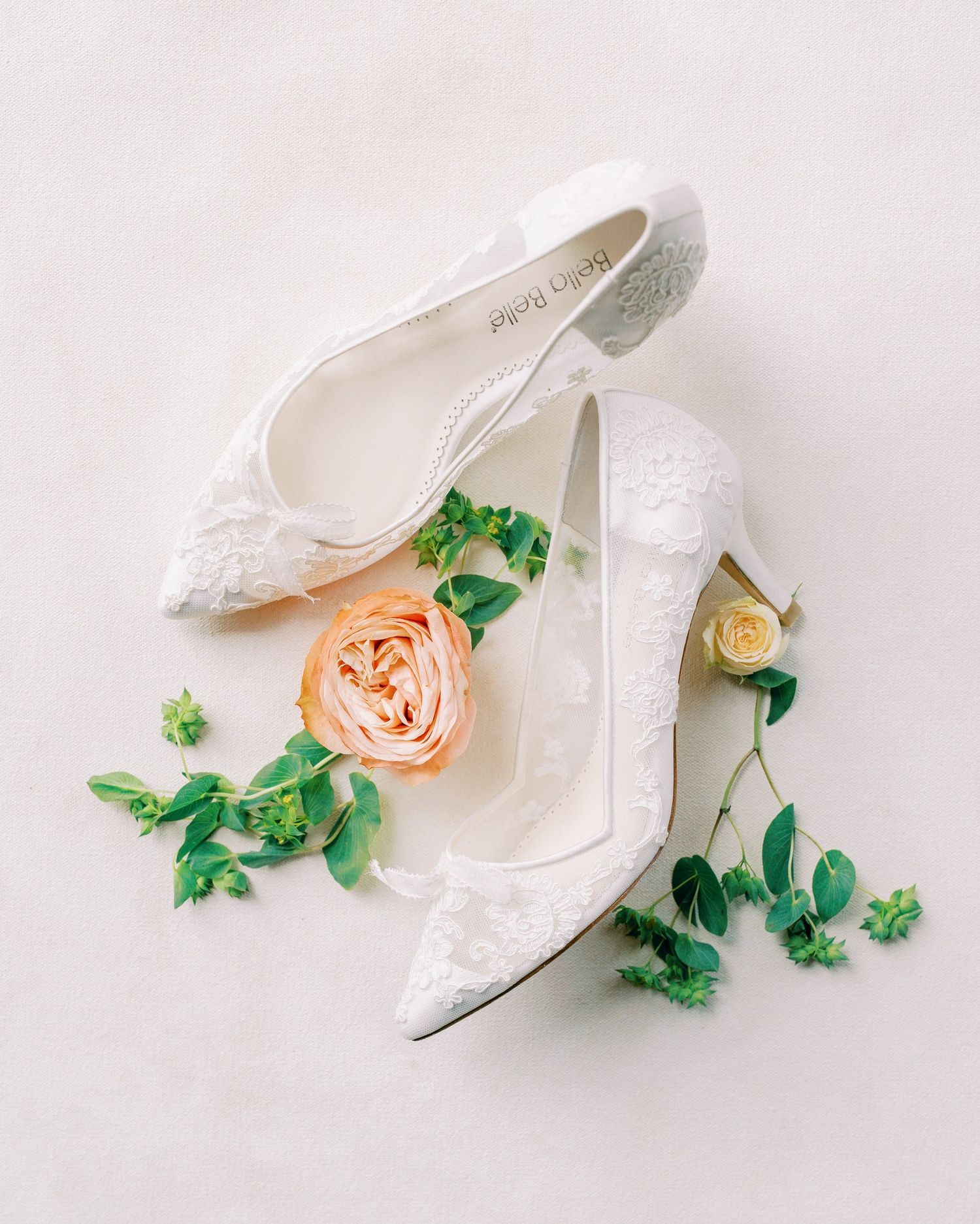 White lace bridal shoes with delicate peach rose and green vine details.