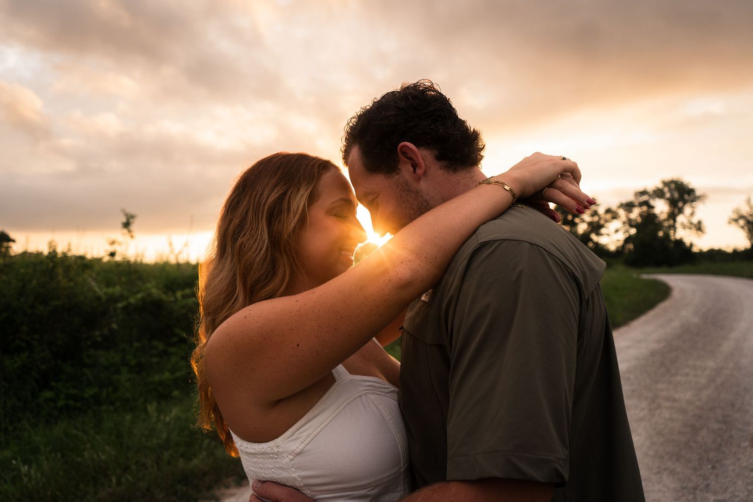 A romantic couple embraces on a country road at sunset creating a silhouette against the warm sky.