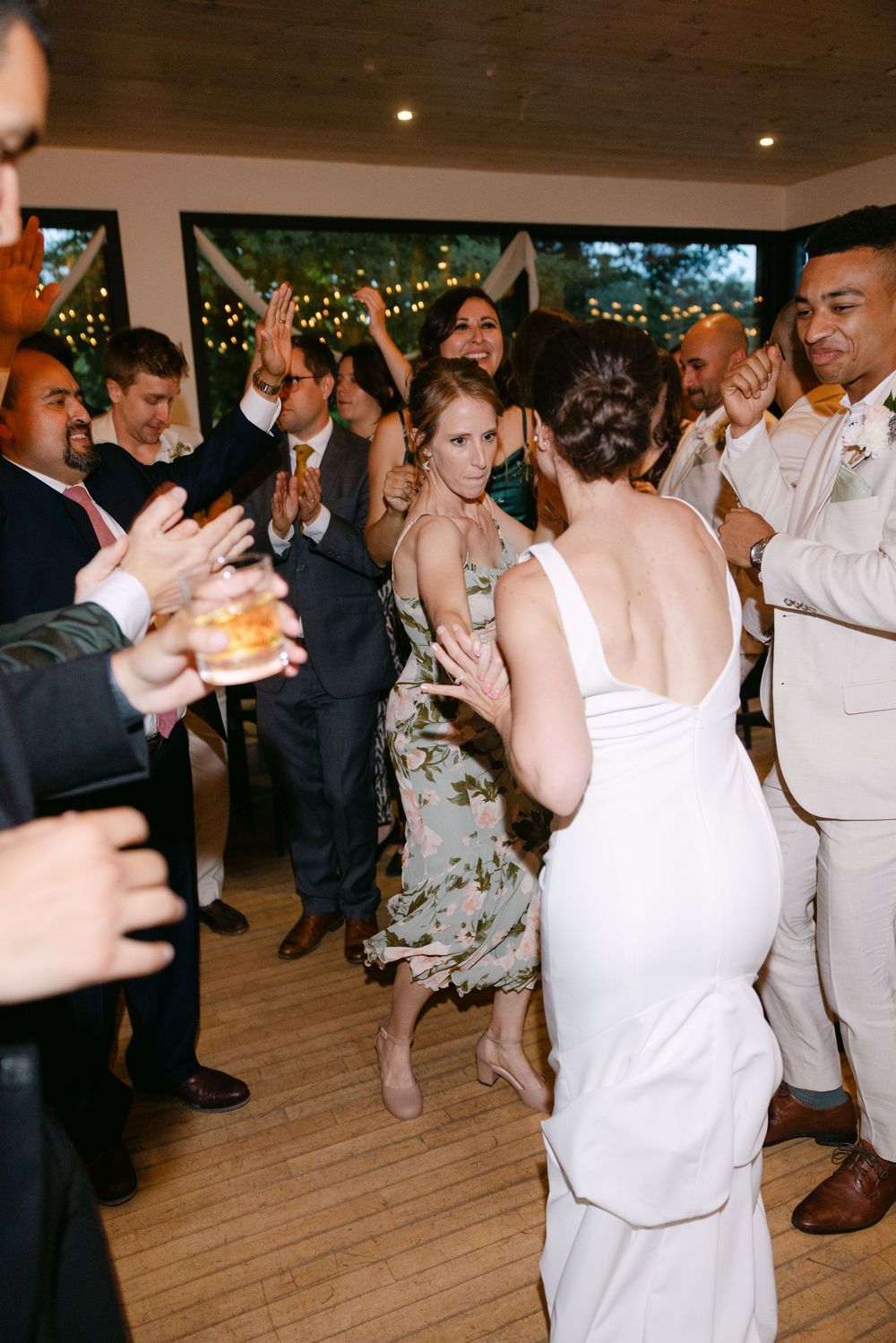 Partygoers dance and celebrate together on a wooden dance floor under indoor lighting.