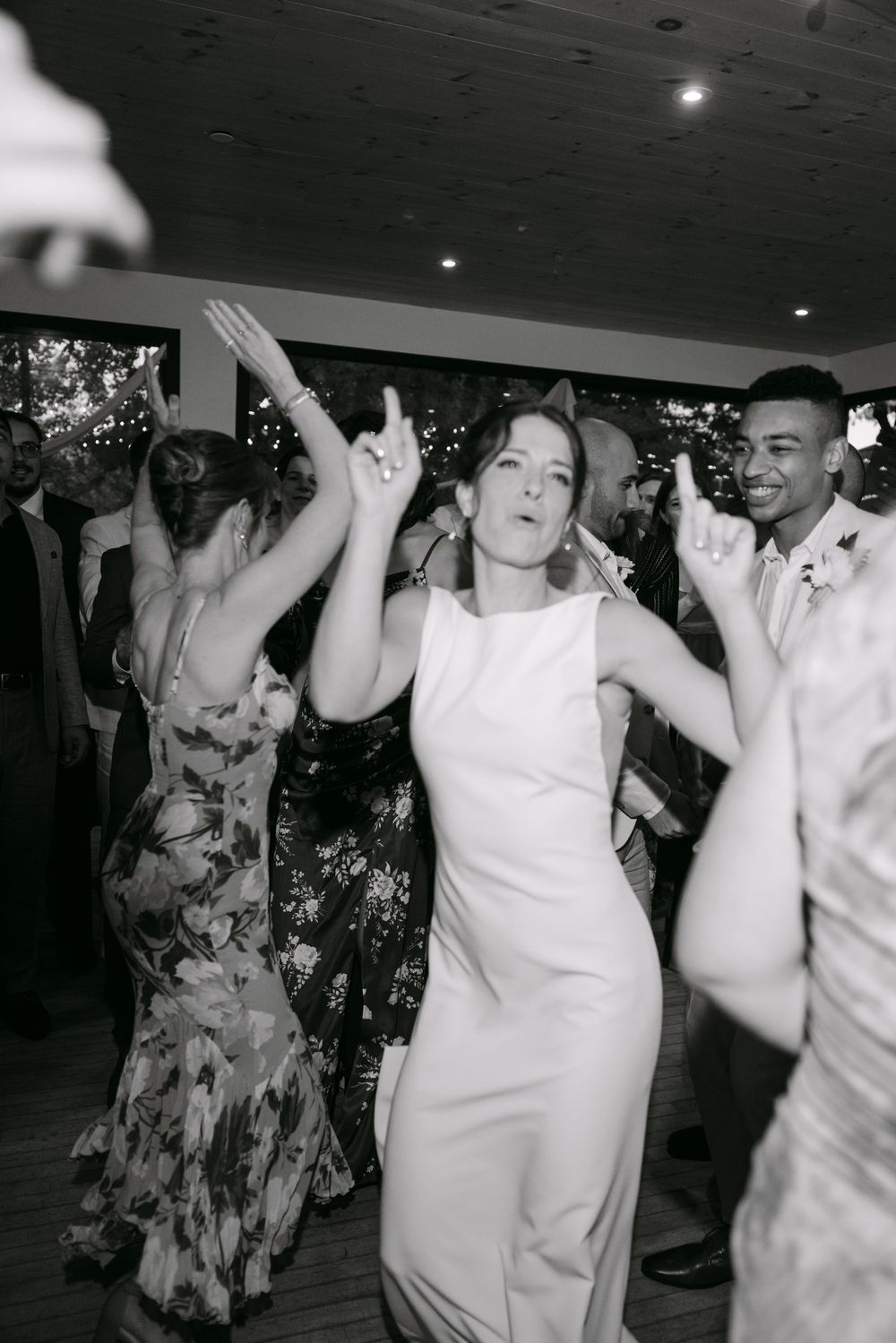 Wedding guests celebrate on the dance floor with energetic dance moves at an indoor reception.