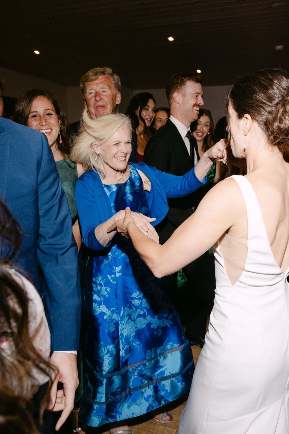 A lively wedding reception scene with guests dancing, including a woman in a blue floral dress and bride in white.
