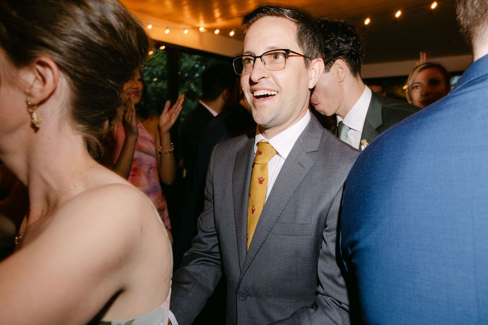 Wedding guests share candid laughter and conversation during an indoor evening reception with warm lighting.