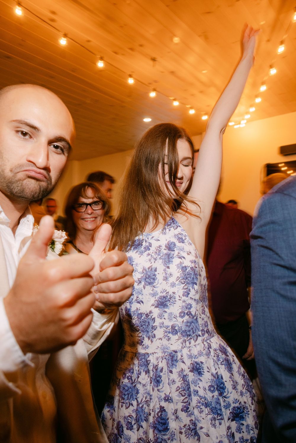 People dancing and celebrating at a party with warm lighting and wooden ceiling.