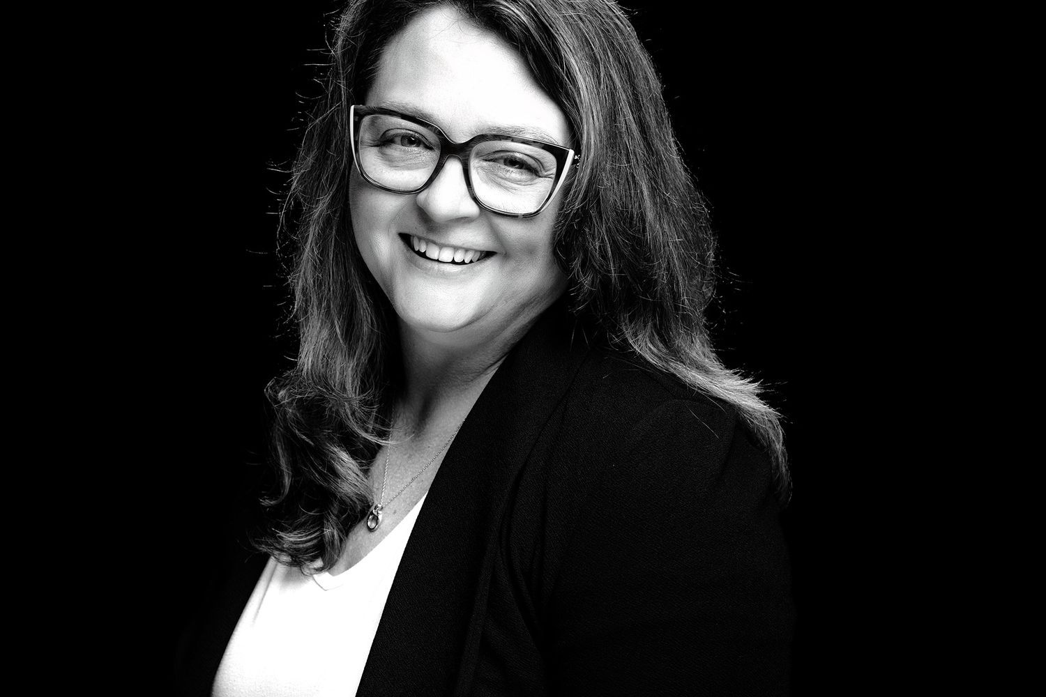 A professional wearing glasses and business attire smiles warmly in a black and white portrait photo.