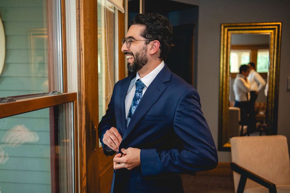 A businessman in a navy suit stands near wooden window frames in an office setting.