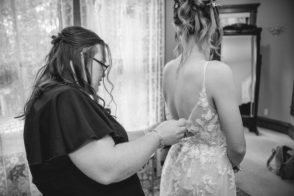 Black and white photo showing final dress adjustments being made by someone wearing dark clothing.