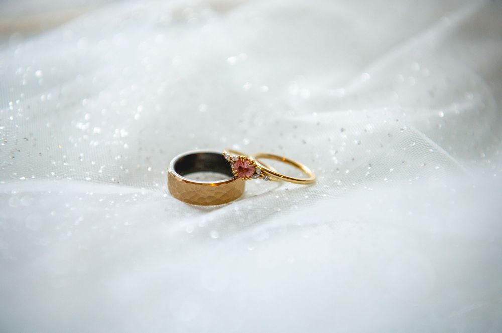 Two wedding rings with delicate floral details resting on soft white fabric with sparkling detail.