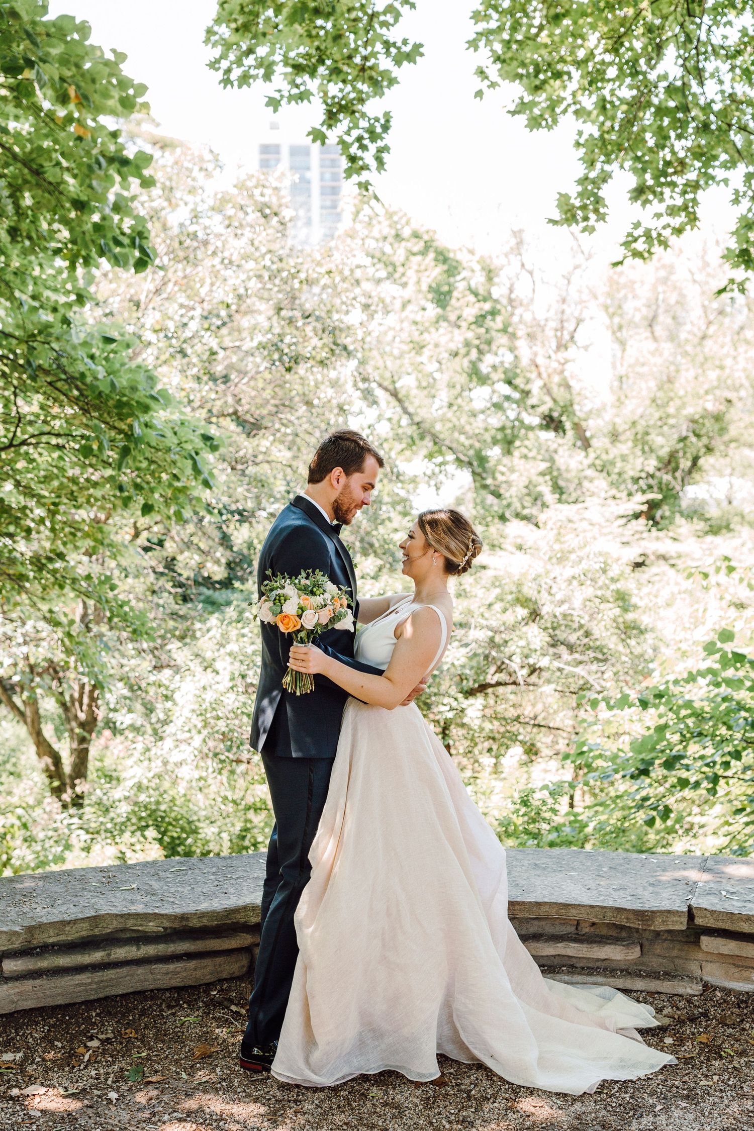 A romantic wedding couple shares an intimate moment on a stone terrace surrounded by lush greenery.