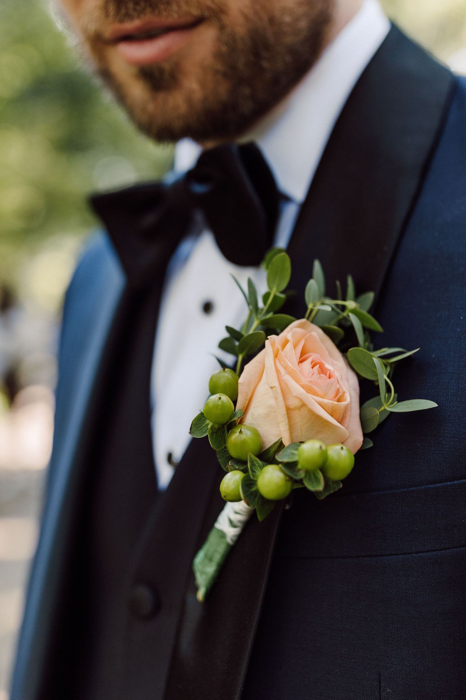 Peach rose boutonniere with green berries pinned to a navy blue suit jacket.