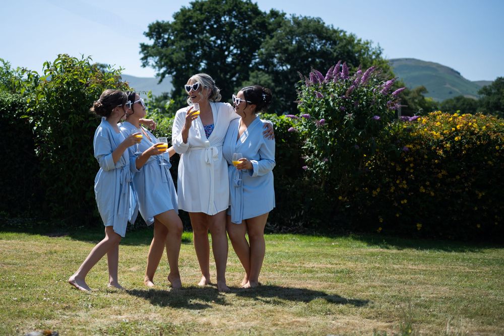 A group in light blue outfits enjoying conversation together on a sunny lawn with flowering bushes in the background.
