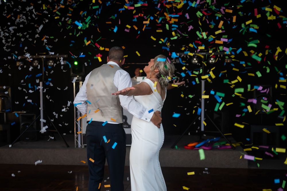 A couple sharing their first dance with colorful confetti falling around them at their wedding celebration.