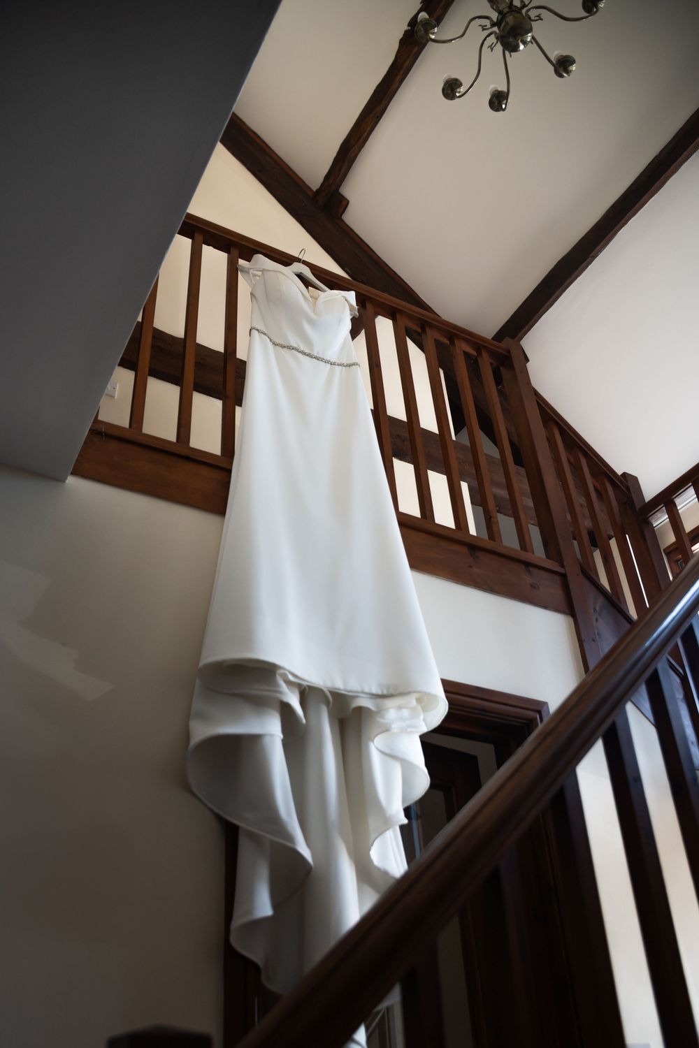 An elegant white wedding dress hanging on dark wooden staircase with dramatic lighting.