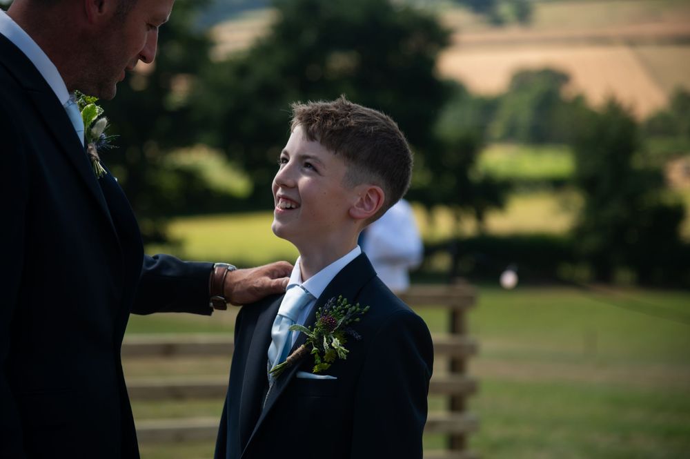 An outdoor moment of formal attire adjustment with greenery in the background.