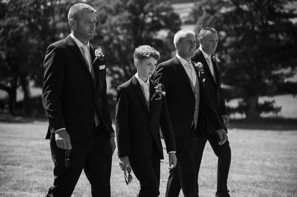 Black and white photo of formal-dressed group walking across a sunny lawn.