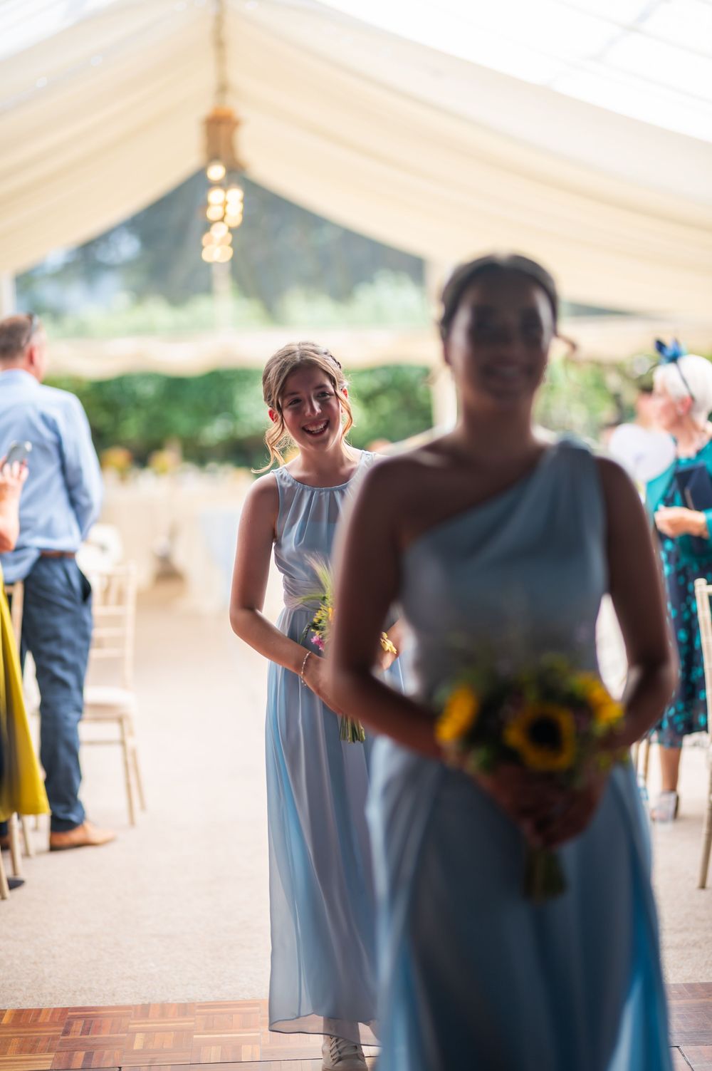 People gathered under a white wedding tent with sunflower decorations.