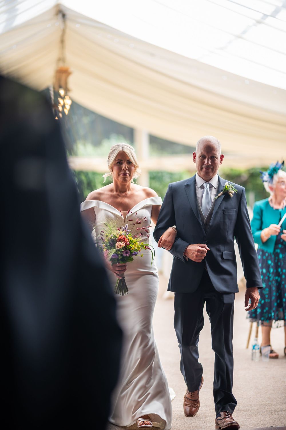Wedding ceremony procession under a white tent with guests watching.
