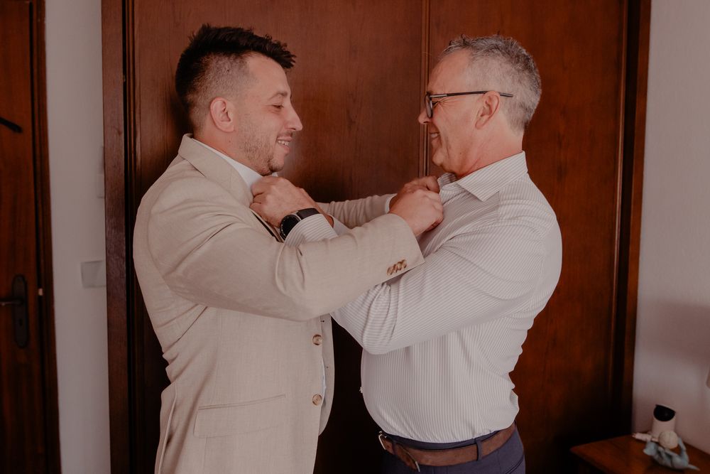 Emotional moment shared between two people in white shirts during wedding preparations.