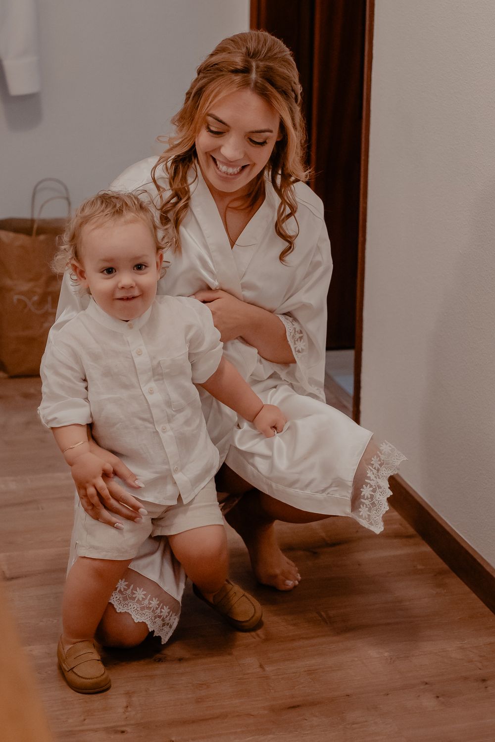 A heartwarming moment in matching white outfits on a wooden floor during wedding preparations.