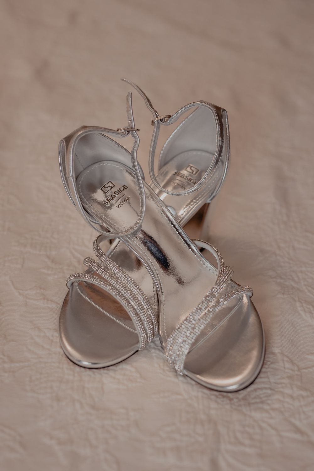 Elegant silver bridal sandals with sparkly straps photographed on a neutral background.