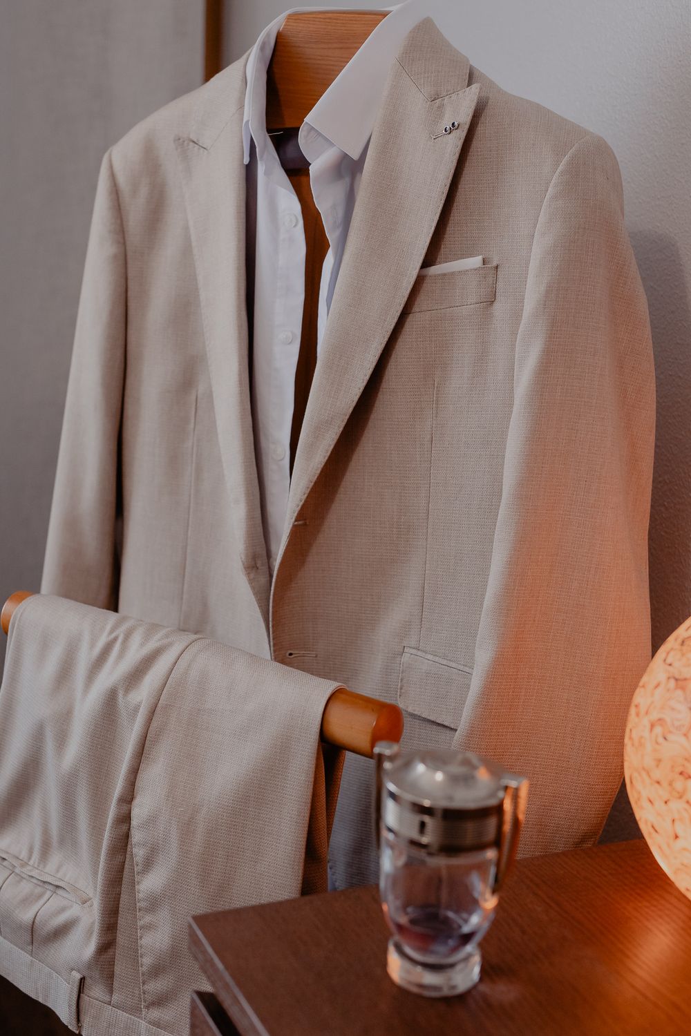 A light beige wedding suit jacket and pants hanging on a wooden hanger.