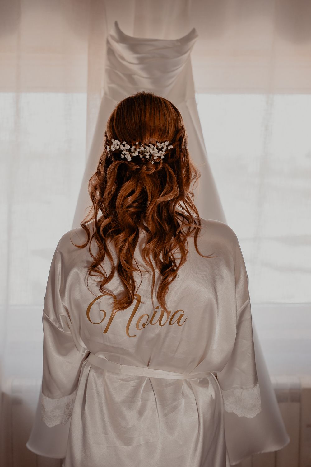 A bridal robe with personalized text and floral hair accessory photographed from behind.