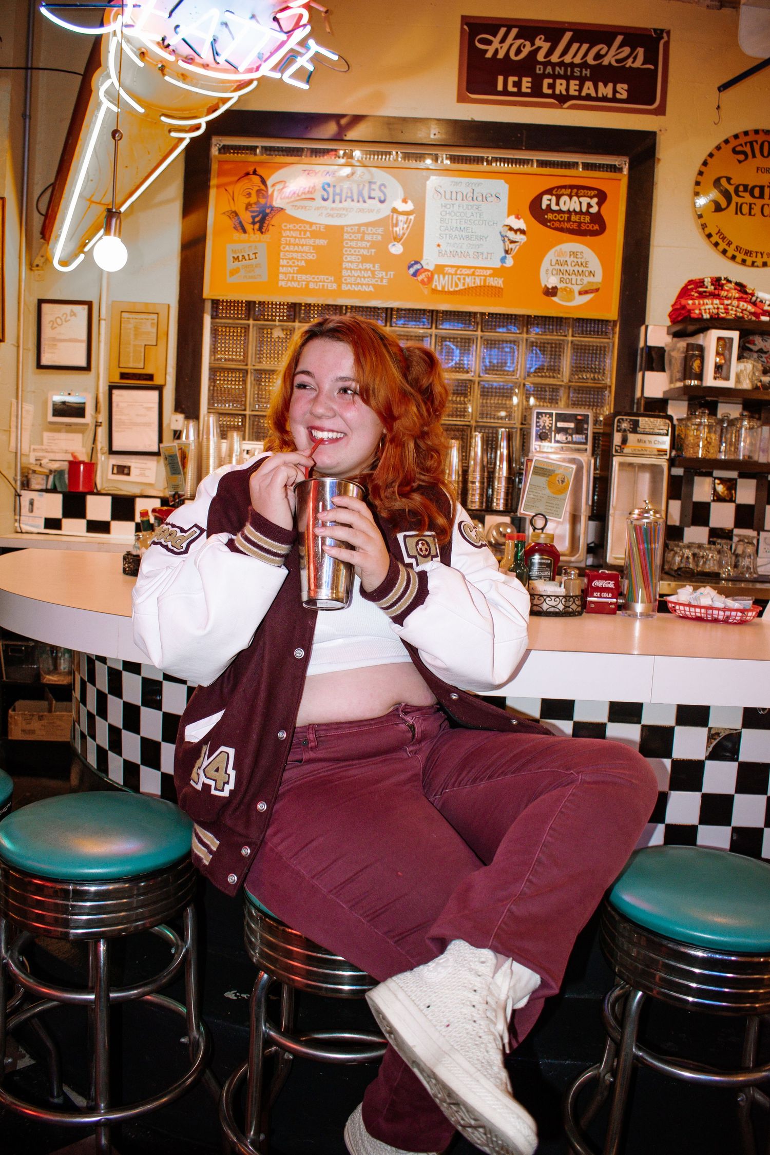 High school senior girl in a maroon letterman jacket sitting in a retro 1950s-style diner booth.