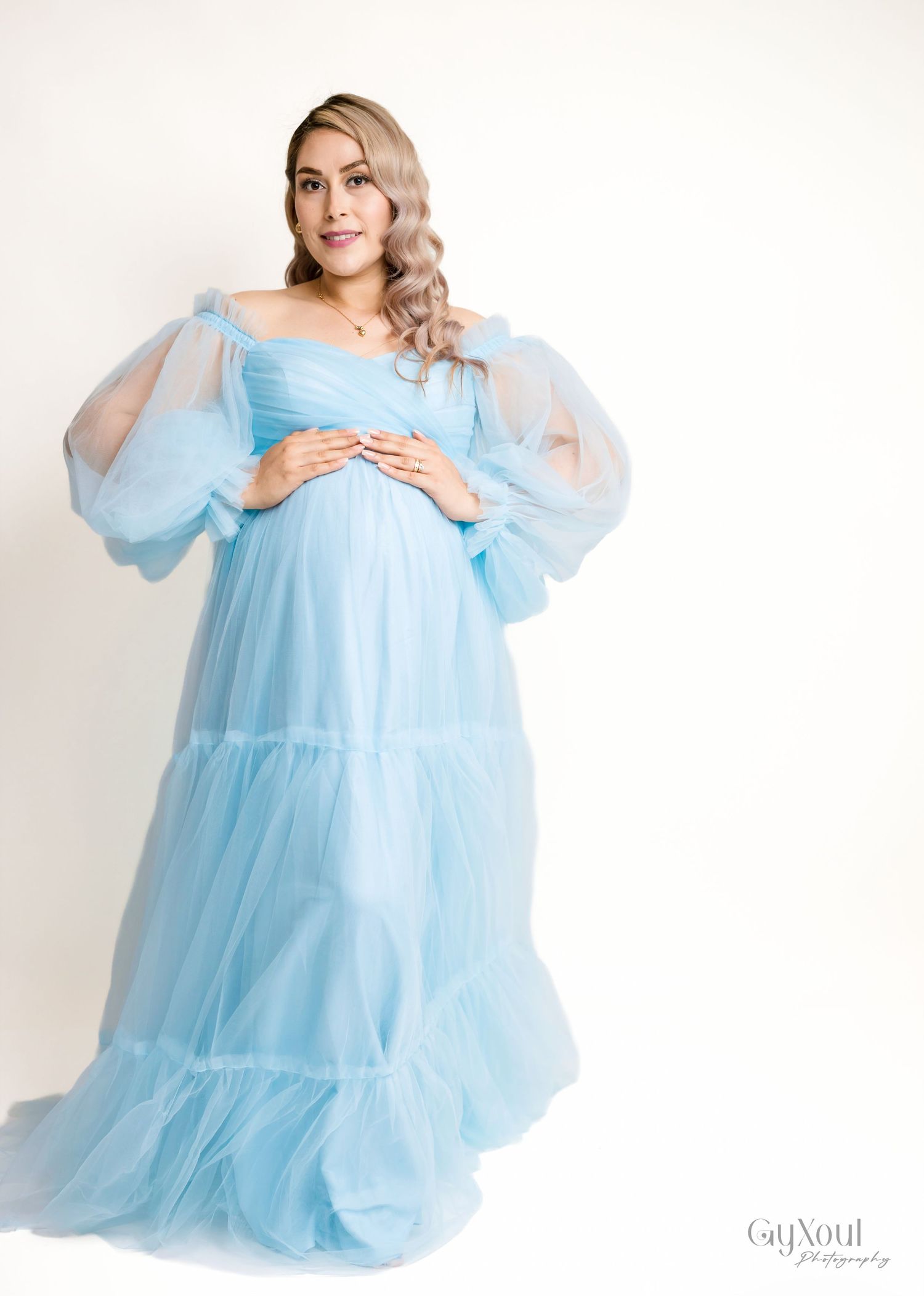 A light blue tulle maternity gown with sheer puff sleeves and empire waistline photographed against a white backdrop.