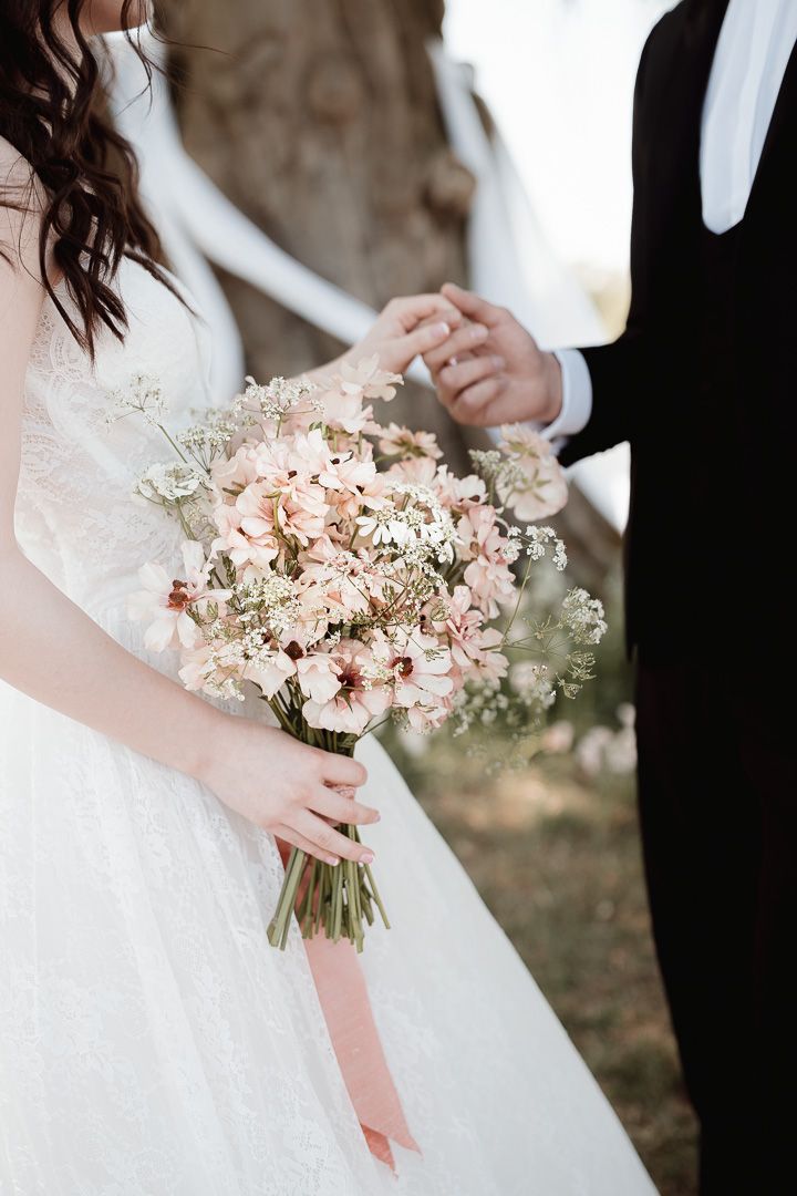 A close-up of a bridal bouquet with blush pink flowers and baby's breath, held against a white wedding dress.