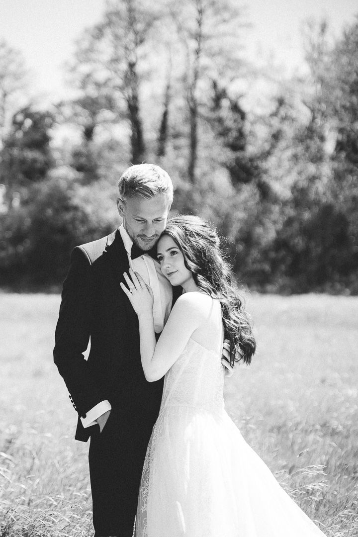 A romantic black and white portrait of a wedding couple embracing in a sunlit meadow.