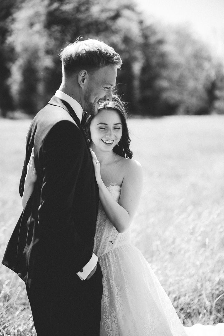 A romantic black and white wedding photo of a couple embracing in a sunny meadow.