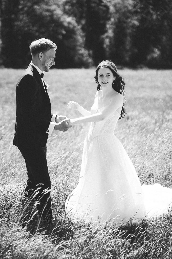 A joyful black and white wedding photo capturing a couple dancing together in a grassy field.