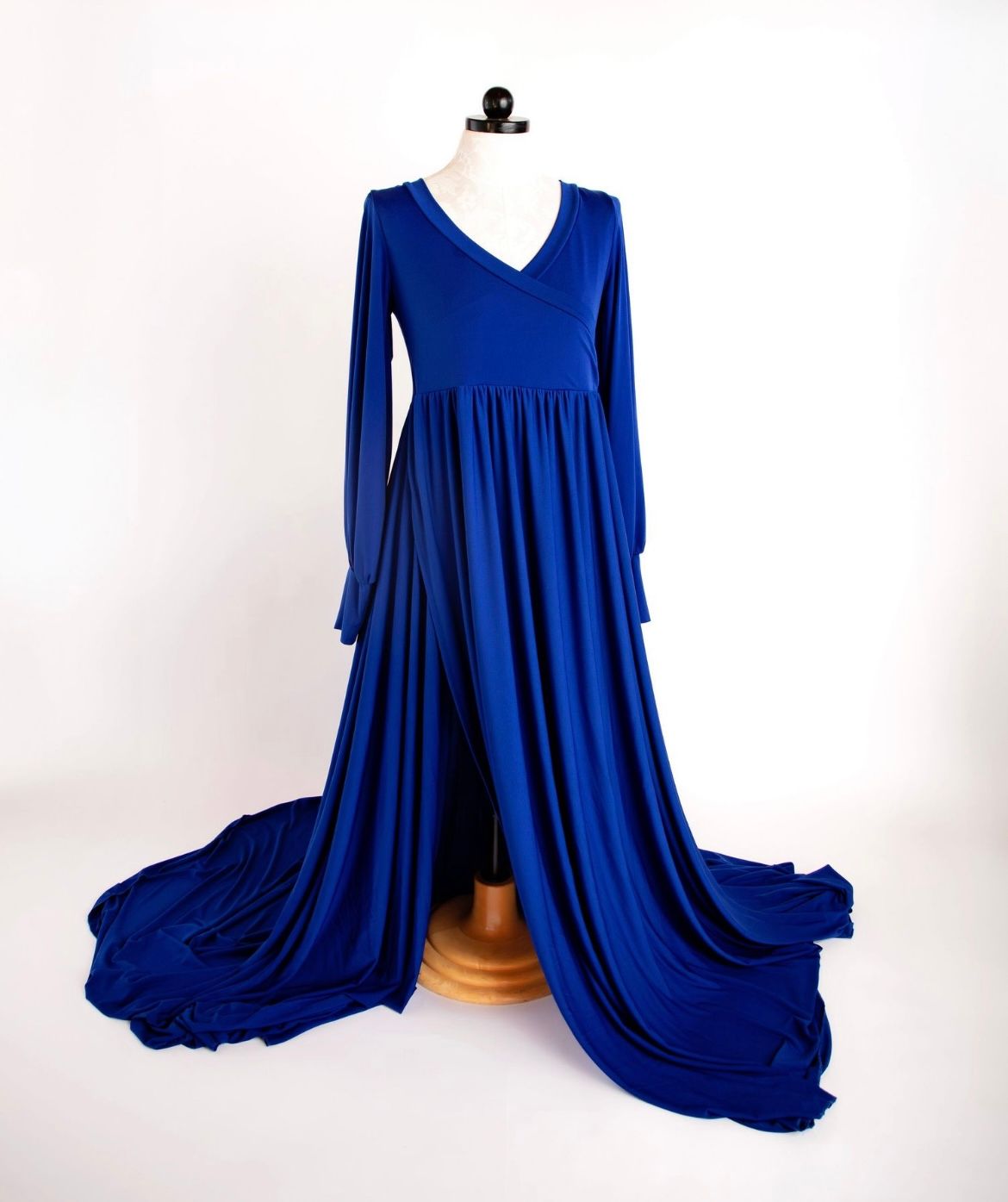 A flowing royal blue dress with long sleeves and dramatic train displayed on a mannequin against white background.