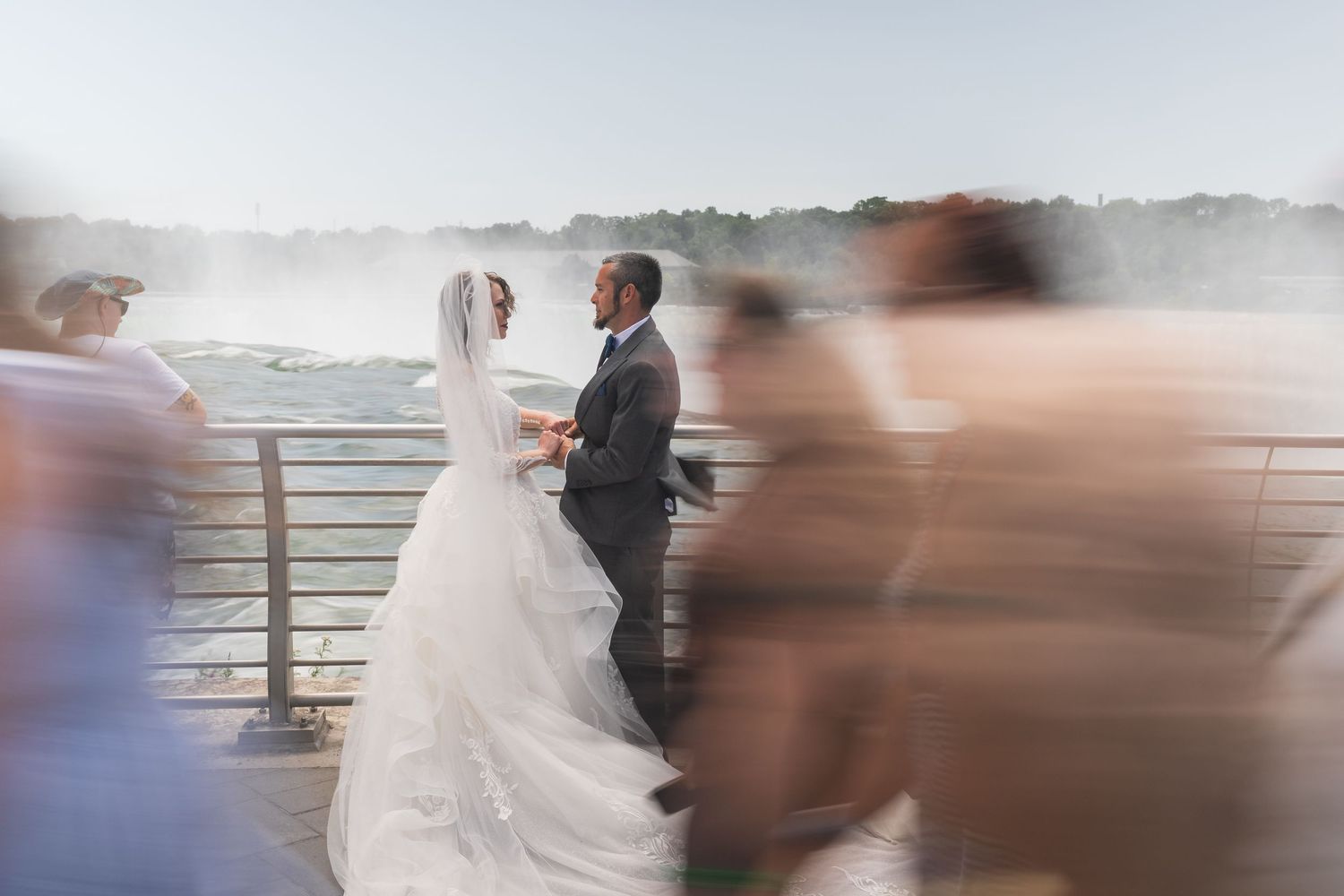A wedding couple walks along a scenic coastal boardwalk as motion blur creates a dreamy romantic effect in this sequence.