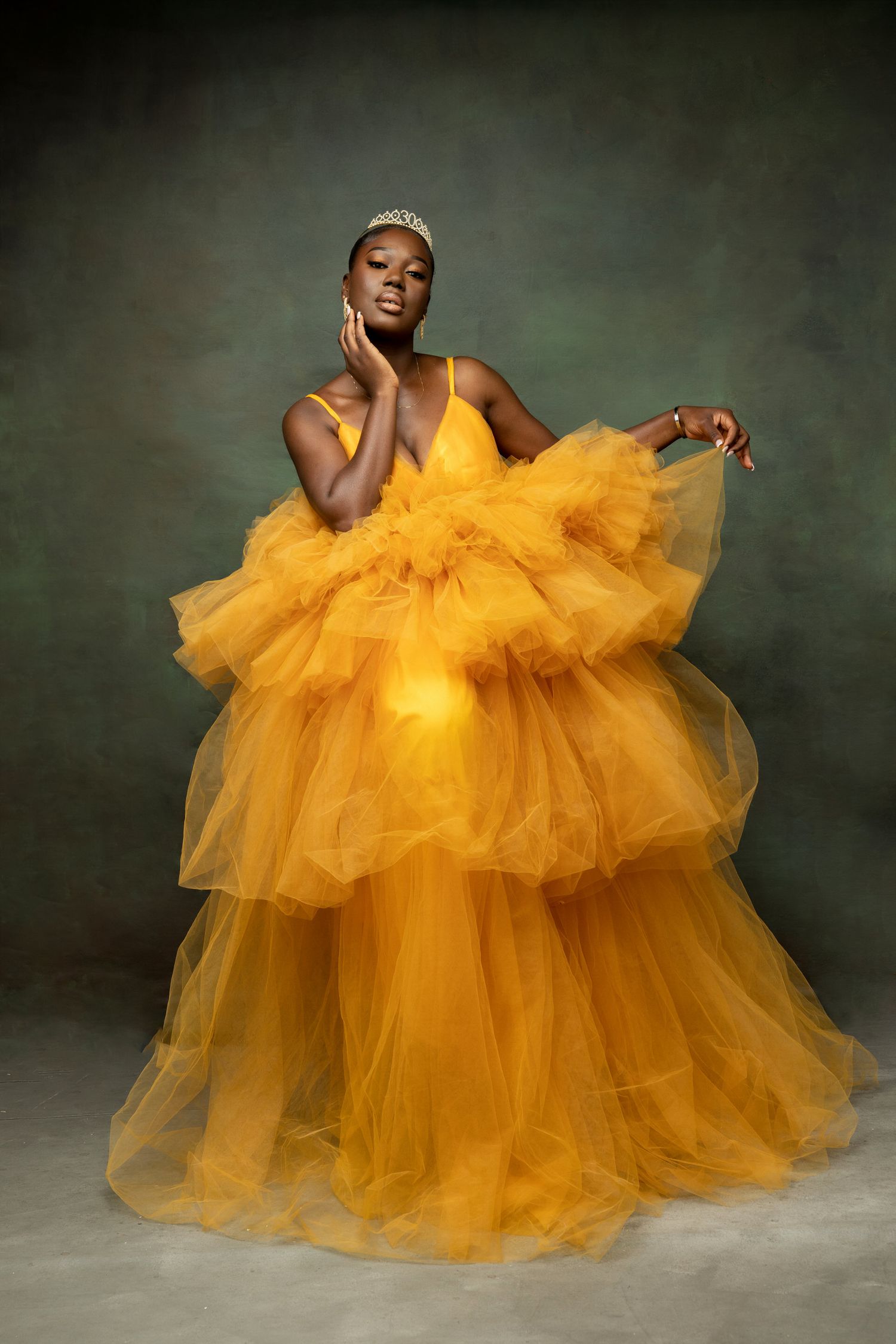 A model poses gracefully in a voluminous yellow tulle gown with tiered ruffles against a dark studio backdrop.