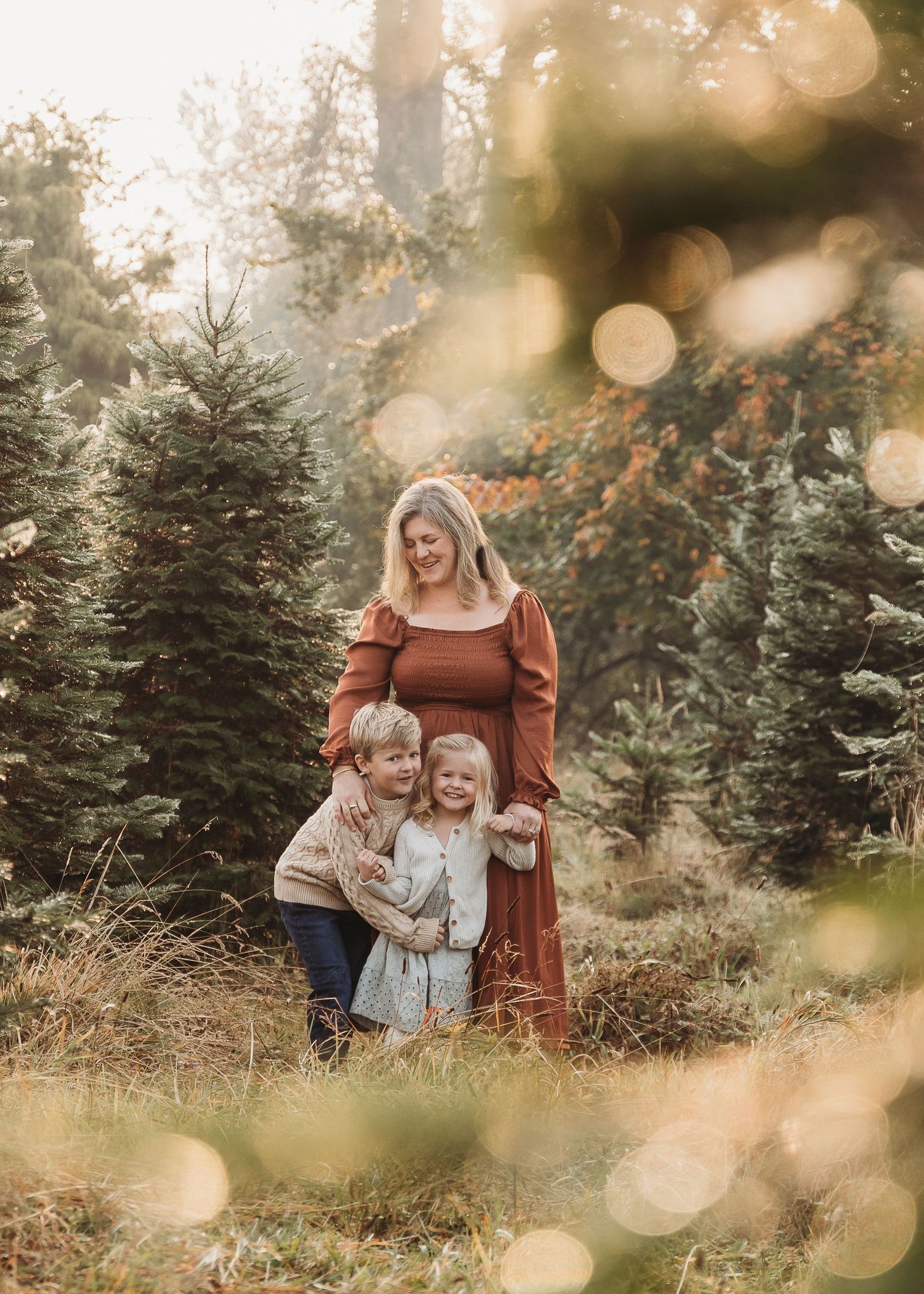 Family sharing tender moments together amidst evergreen trees at sunset with magical bokeh lighting effects.