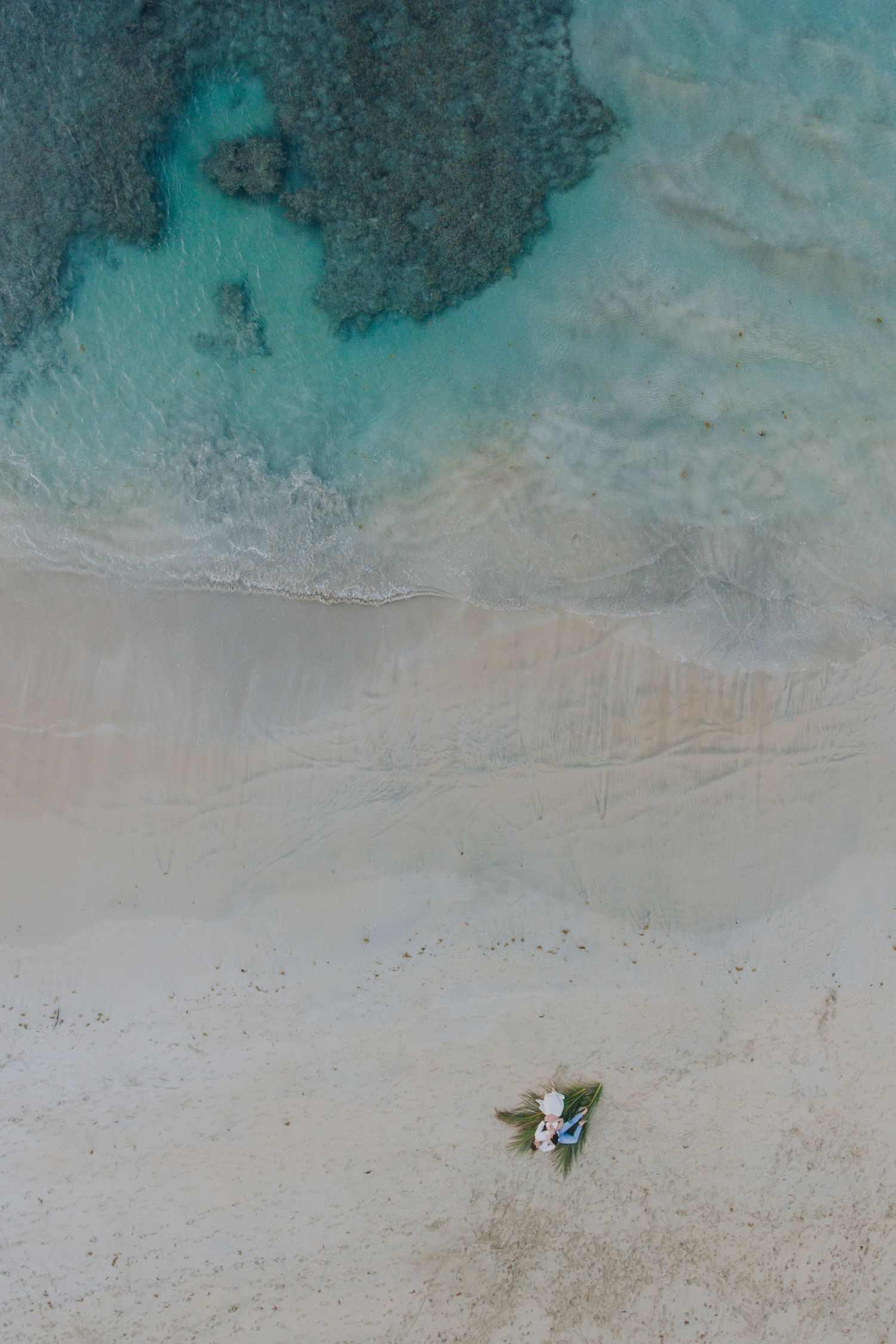 Aerial drone shot of a beach with turquoise waters and two small figures on white sand.