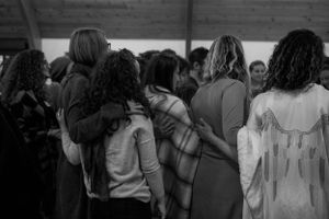 A group stands together in an intimate gathering, photographed from behind.