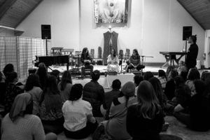 Musicians perform in a church-like venue with audience members seated on the floor.