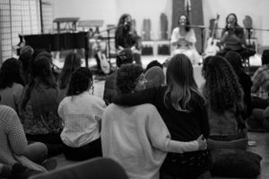 People seated on the floor watching a performance in a community space.